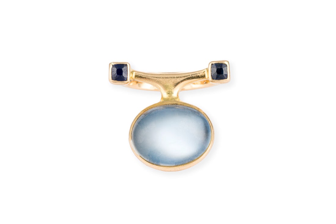 ASYMMETRISCHER DESIGN RING: ASYMMETRISCHER DESIGN RING GG 750. Ringmass: ca. 50. Ges.-Gew.: ca. 6,7 g. Ring, besetzt mit einem zentralen Mondstein-Cabochon von ca. 6.10 ct., flankiert von zwei Saphir-CarrEs zus. ca. 0.25 ct.