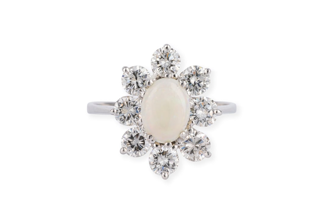 OPAL ENTOURAGE RING: OPAL ENTOURAGE RING WG 750 (getestet). Ringmass: ca. 55,5. Ringkopfmasse: ca. 16,8 x 14,0 mm. Ges.-Gew.: ca. 4,4 g. Ring, besetzt mit einem zentralen, ovalen Opal-Cabochon von ca. 1.00 ct. und einem