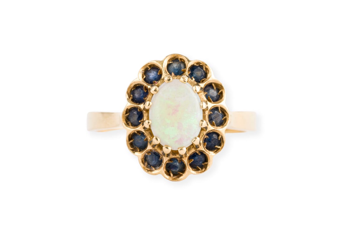 OPAL SAPHIR RING: OPAL SAPHIR RING GG 750. Ringmass: ca. 56. Ringkopfmasse: ca. 14,3 x 12,6 mm. Ges.-Gew.: ca. 4,9 g. Ring, besetzt mit einem zentralen Opal von ca. 0.95 ct. und einem Kranz aus Saphiren.