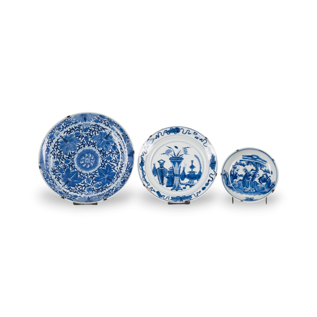 DREI BLAU-WEISSE TELLER: THREE BLUE AND WHITE DISHES China, Qing dynasty Porcelain. D. 14.5-24 cm. Including a saucer decorated with a figural scene, with a 'Kangxi nianzhi' mark and a Lempertz label to the base, a dish decor