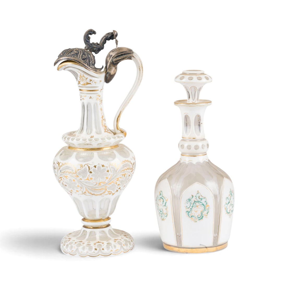 | KANNE UND KARAFFE IM HISTORISMUS-STIL: KANNE UND KARAFFE IM HISTORISMUS-STIL Wohl Deutsch, 20. Jh. Farbloses Glas mit milchweissemUeberfang, teilw. polychrom bemalt, Goldstaffage, Silbermontierung. H. 27,5-35 cm. Teilw. mit Monogramm 'JBB'