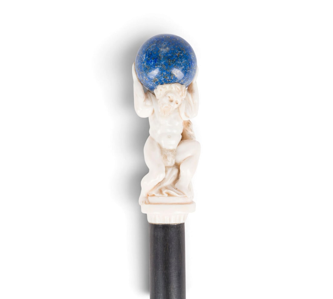 | FIGUeRLICHER SPAZIERSTOCK MIT ATLAS: FIGURAL WALKING STICK WITH ATLAS 19th century Wood, steel, ivory, lapis lazuli. Total length 90 cm. Damaged.FIGUeRLICHER SPAZIERSTOCK MIT ATLAS 19. Jh. Holz, Stahl, Elfenbein, Lapislazuli. Ges.-L. 90