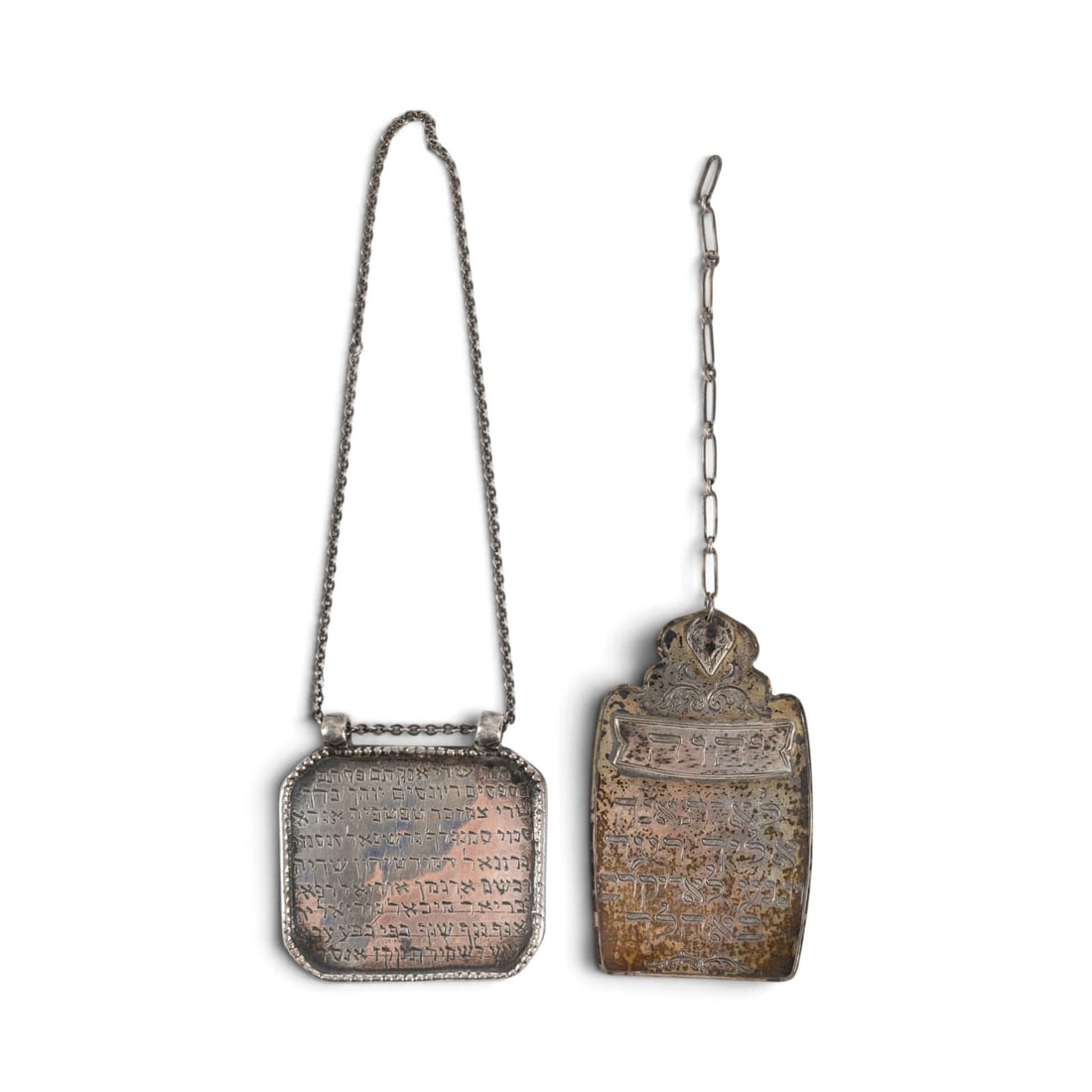 | ZWEI TORASCHILDER: TWO TORASHIAN SHIELDS 19th/early 20th Century Silver, approx. 53 g. 7.5 x 4.5 cm / 5 x 5.5 cm (excluding chains). Shield-shaped, one with a relief border, engraved Hebrew inscriptions, on chains. Sign