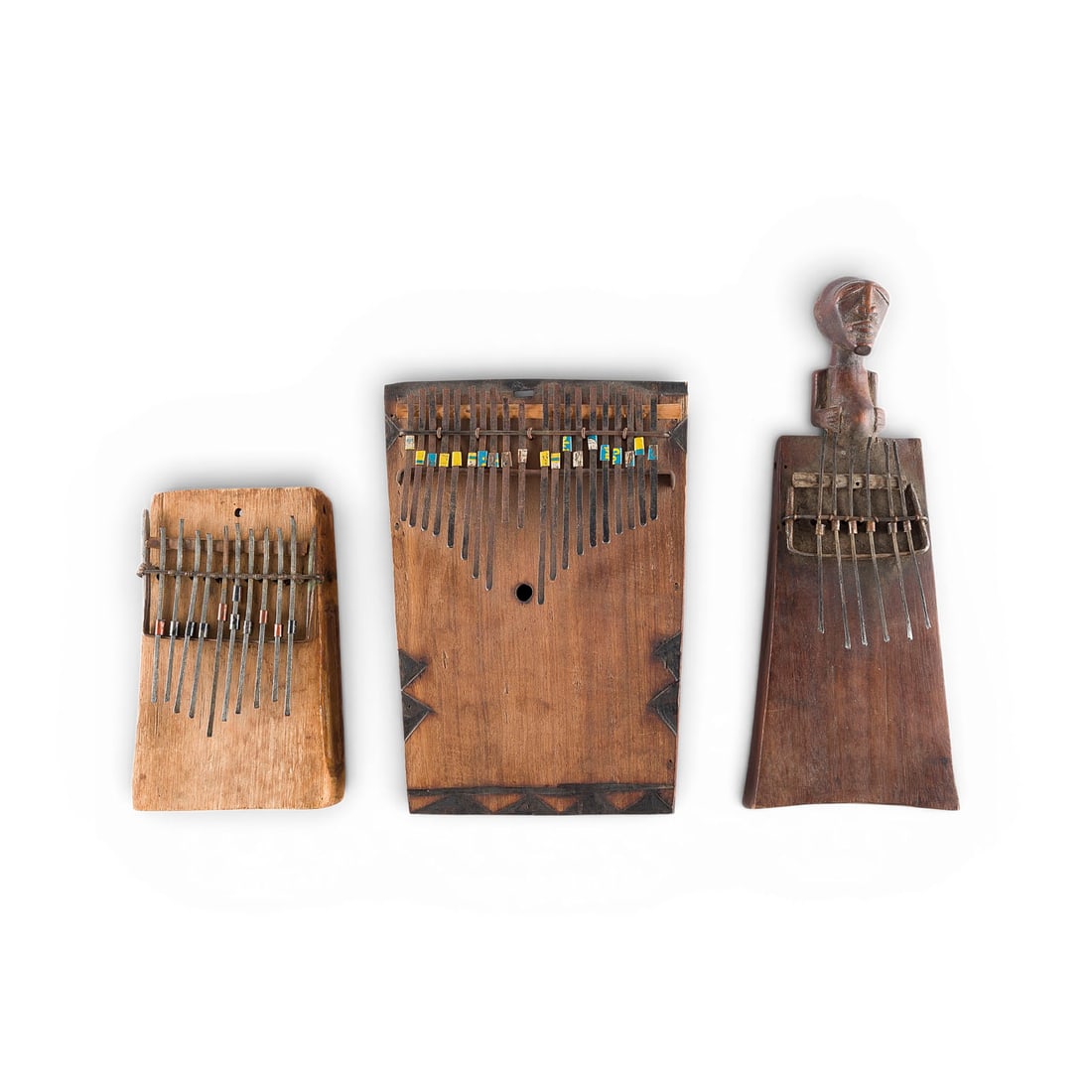 | KONVOLUT VON DREI KALIMBAS / MBIRAS: SET OF THREE KALIMBAS / MBIRAS Africa, probably Tanzania, 20th century Wooden soundboard, freely vibrating metal tongues, one with a carved head at one end. L. 18, 24.5, 29.5 cm. Three traditional