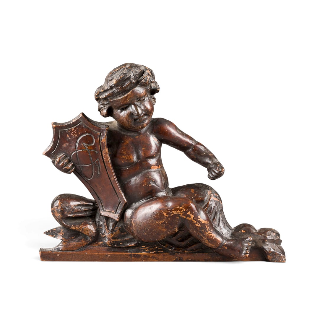 | SITZENDER PUTTO MIT WAPPEN: SEATED PUTTO WITH COAT OF ARMS German, 18th century Wood, sculpted, dark stained. H. 33, W. 40, D. 10 cm, weight approx. 1.94 kg. Partially bumped and damaged.SITZENDER PUTTO MIT WAPPEN Deutsch, 18. J