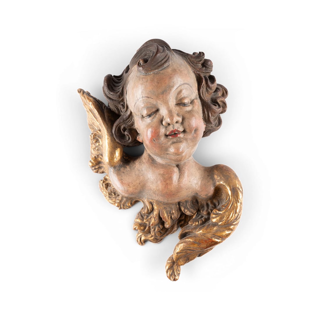 | GROSSER GEFLUeGELTER PUTTOKOPF: LARGE WINGED CHERUB HEAD South German, 18th century Wood, carved in the round, polychromed and gilded; flattened and hollowed out at the back. H. approx. 44, W. 36, D. 20 cm. Minor chips and damage; l