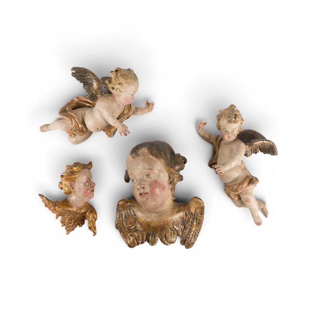 | KONVOLUT VON VIER FIGUREN: ZWEI GEFLUeGELTE PUTTEN UND ZWEI ENGELSKOePFE: GROUP OF FOUR FIGURES: TWO WINGED PUTTI AND TWO CHERUB HEADS South German or Alpine region, 17th and 18th centuries Wood, carved in the round, polychrome and gilt finish, flattened backs. H. 31/32, 21