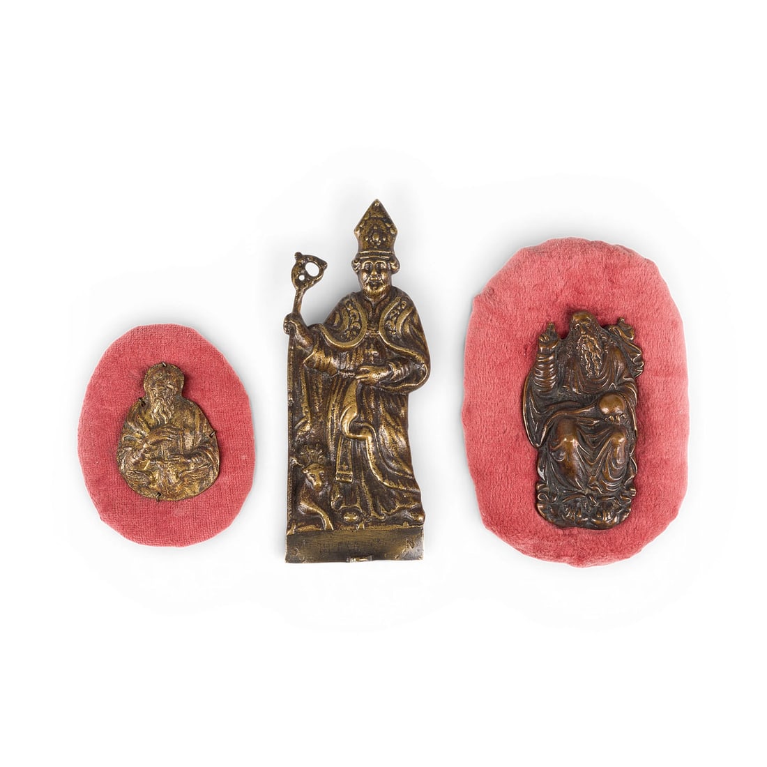 UNBEKANNTER BILDPLASTIKER | KONVOLUT VON DREI BRONZERELIEFS: HEILIGER BISCHOF, JOHANNES UND GOTTVATE: UNKNOWN SCULPTOR Active 19th/20th century GROUP OF THREE BRONZE RELIEFS: SAINT BISHOP, SAINT JOHN, AND GOD THE FATHER Bronze with gold patina; two mounted on red velvet. Heights: 6 cm, 9.5 cm, 16 cm.