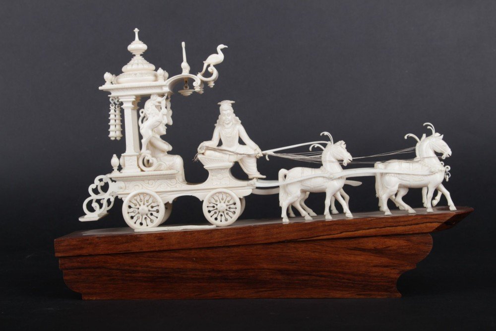 Decorative ivory sculpture of a nobleman going on the: India, 20th-30th years of the 20th century, detailed carving captures a chariot drawn by four with a nobleman, and a bow with an arrow on the right side of chariot, silver thread, wooden pedestal, siz