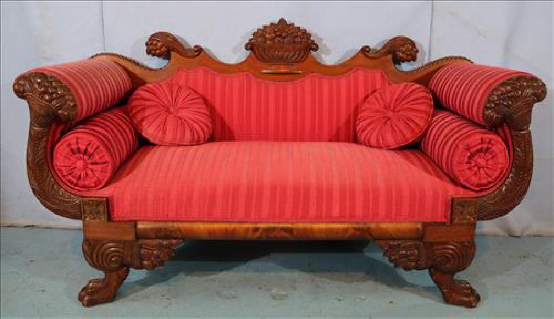 Mahogany Empire love seat with carved fruit basket: Mahogany Empire love seat with carved fruit basket crown, horn of plenty carved arms, claw feet and red upholstery, 37 in. T, 64 in. W, 22 in. D.
