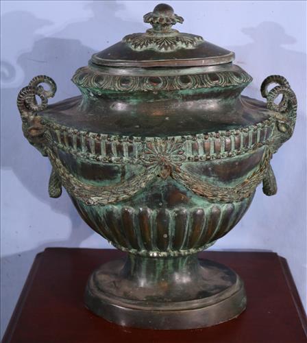 Bronze capped urn with ram heads: Bronze capped urn with ram heads, 17.5 in. T, 15.5 in. W, 10 in. D.