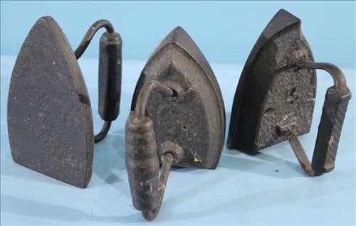 Set of 3 Black Smoothing Irons or Doorstops: Set of three antique black cast iron smoothing irons, or sad irons, each with a traditional triangular base and curved handle. These utilitarian pieces, once essential for pressing garments, now make