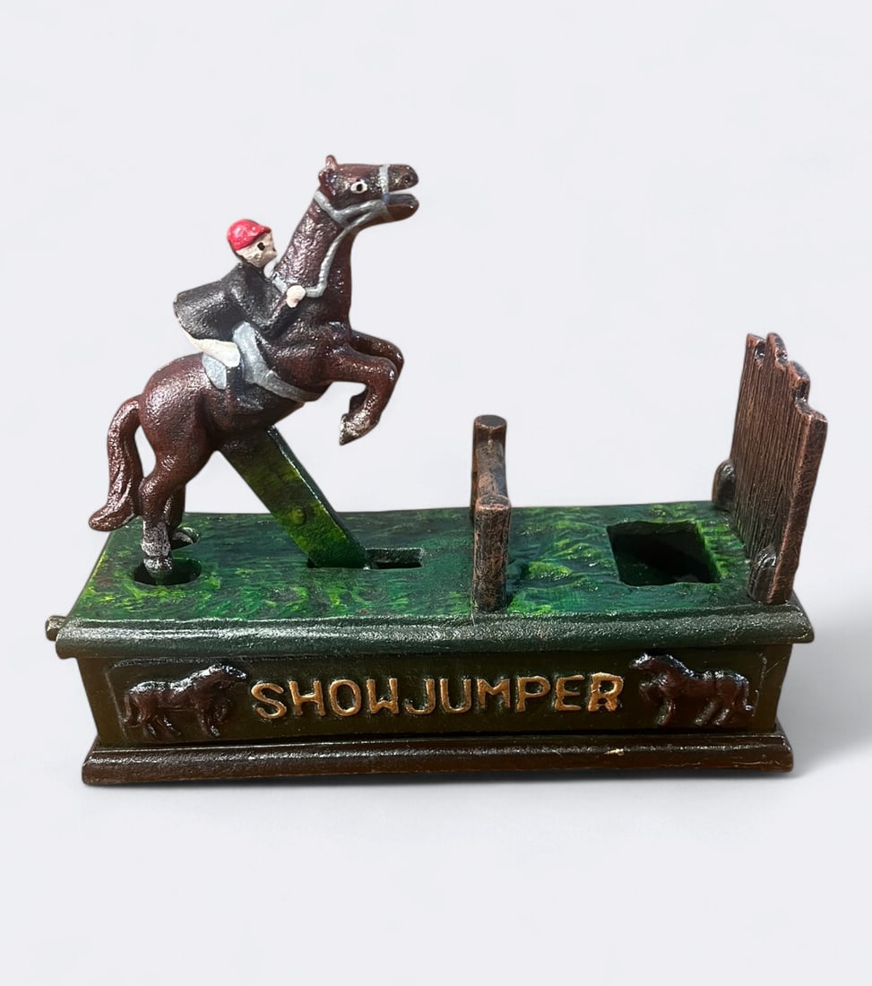 Cast Iron Mechanical Bank, "Showjumper": Painted cast iron mechanical bank featuring a show jumper on horseback, rider in red cap and hunting jacket, mounted above a green painted base makred "SHOWJUMPER" with relief horse motifs on either s