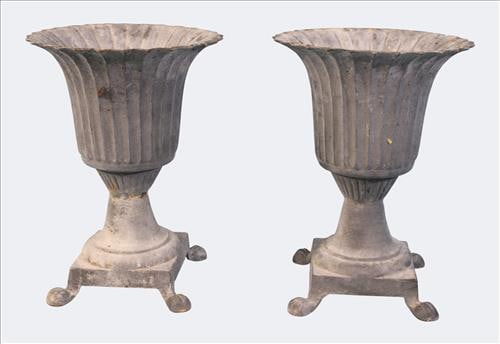 Pair of Gray Cast Iron Garden Urns: Pair of gray cast iron garden urns, each with scalloped and flared rim over a ribbed body, raised on square stepped base with paw-style feet. Both retain an aged, weathered surface, showing an appeali