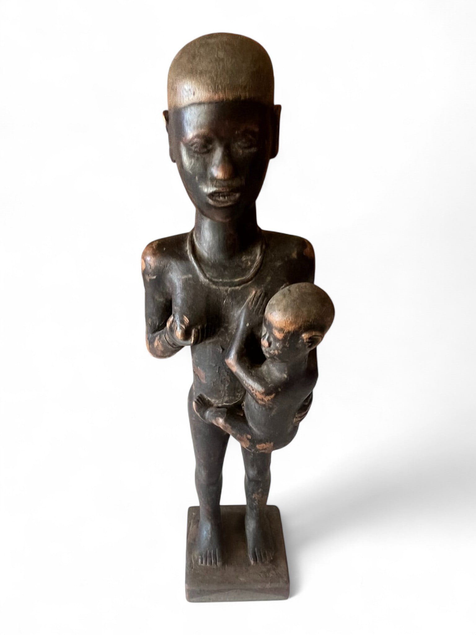 African Carved Wooden Mother and Child Figure: Graceful hand-carved African wooden figure depicting a standing mother nursing her child, rendered with simplified yet expressive form and smooth surface patina. The composition emphasizes maternal st