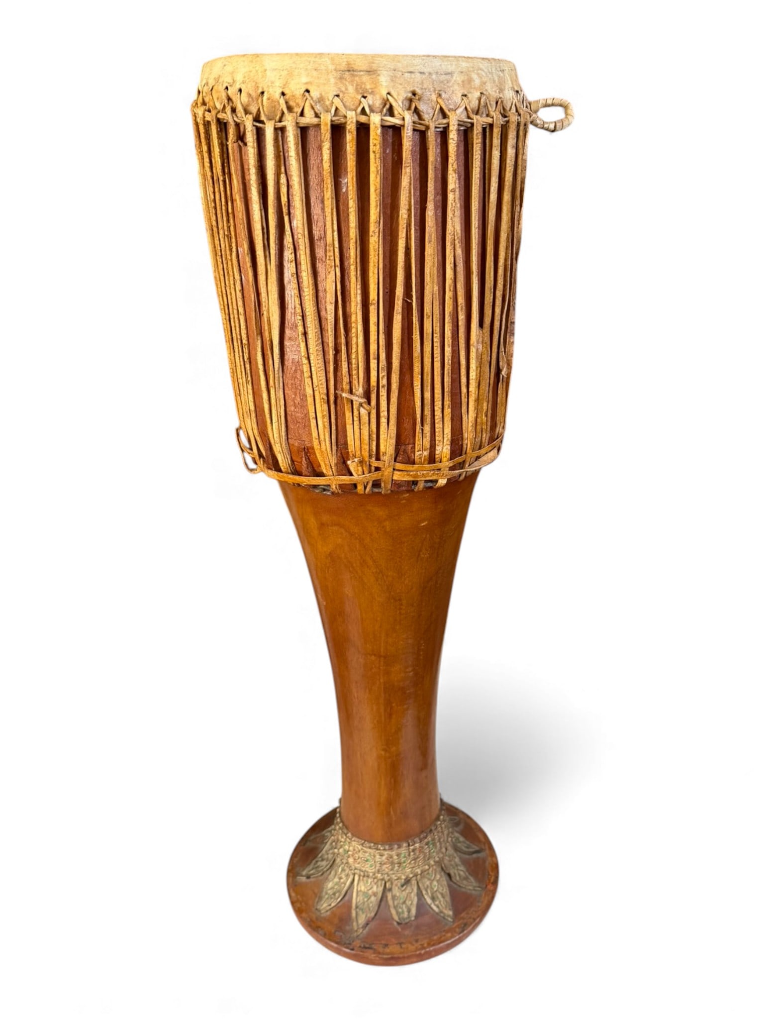 African Goblet Drum with Hide Head and Carved Base: A tall African goblet drum (djembe-type form) with stretched hide head and braided hide lacing, raised on an elongated carved wooden body with painted foliate decoration at the foot. Natural wear from