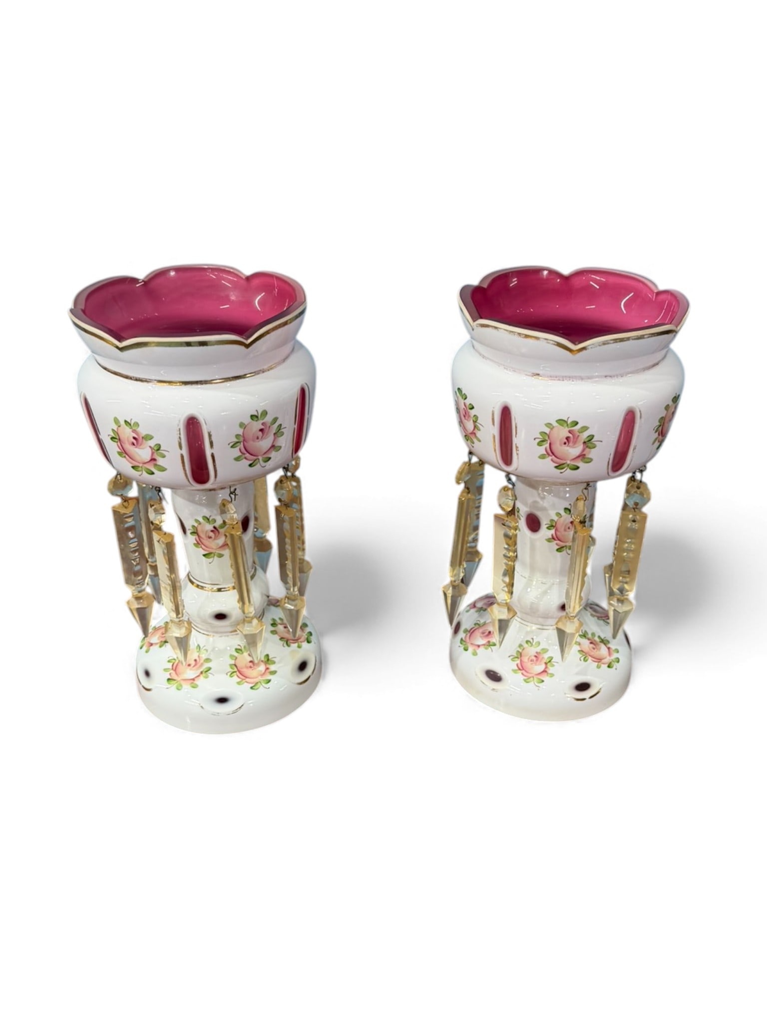 Pair of Bohemian-Style Cranberry Glass and Enameled Lustres, late 19th to early 20th century: Decorative pair of glass lustres with cranberry-colored bowls featuring scalloped rims accented with gilt borders, raised on white opaline-style glass columns hand-painted with floral sprays and gilt
