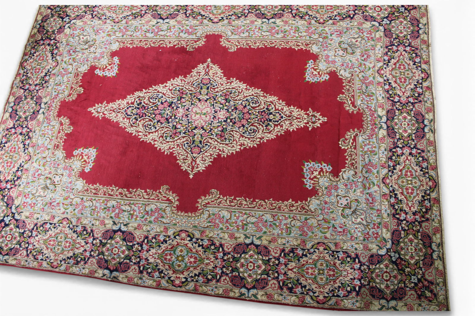 Large Red and Gold Kerman H.K. Wool Rug: Large Persian Kerman H.K. Wool Rug — A finely woven Persian Kerman rug featuring a rich red field centered with an elaborate floral medallion in navy, ivory, rose, and pale celadon tones. The wide n