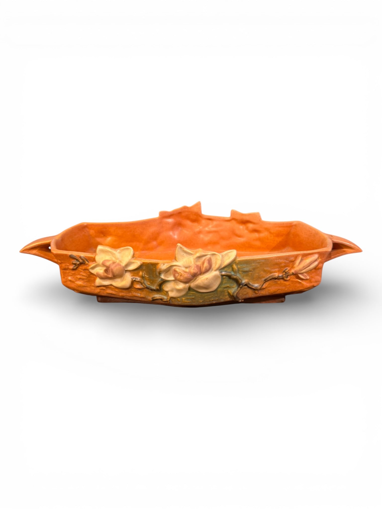 Roseville Magnolia Bowl, American, ca. 1943–1945: A finely modeled Roseville Pottery bowl from the popular Magnolia line, featuring an elongated oval form with gently scalloped rim and integral handles. The exterior is decorated in high relief with b