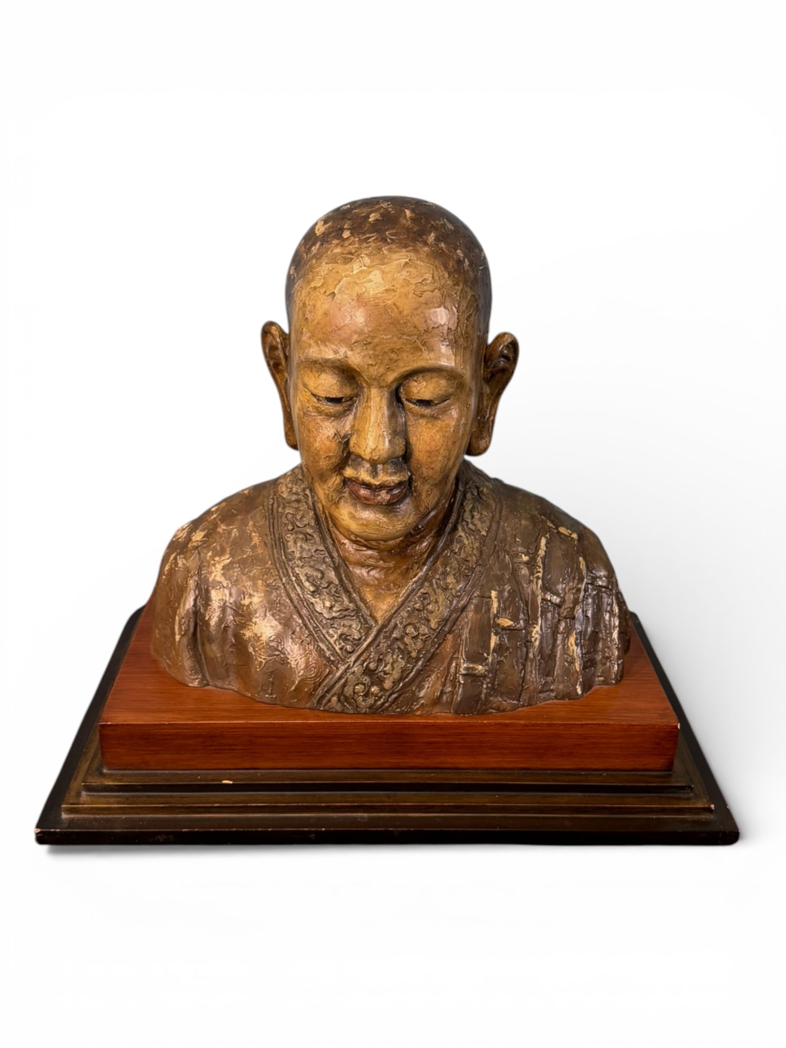 Asian Sculptural Bust in the Buddhist Manner: Composite sculptural bust depicting a serene male figure in the Buddhist manner, shown with shaved head, elongated ears, and downcast eyes conveying contemplative calm. The figure wears draped robes