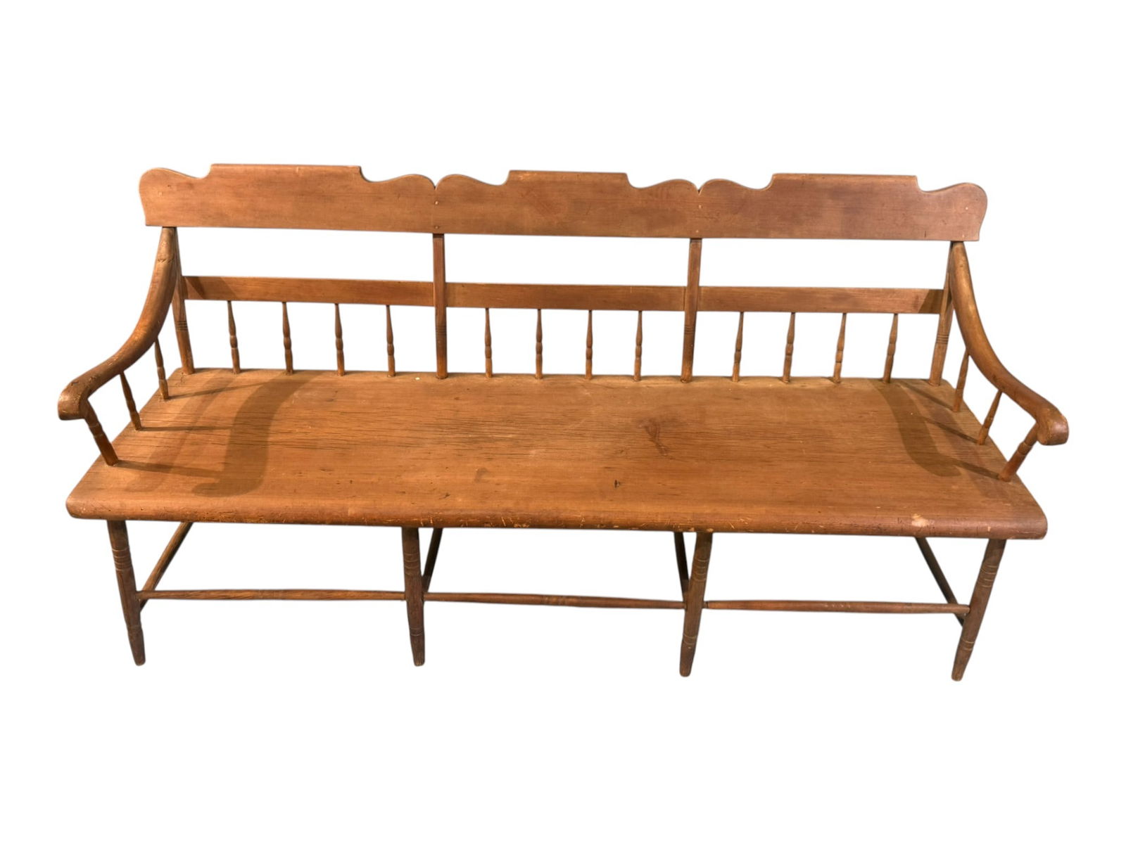 American Primitive Pine Bench / Settle, 19th Century: Large American primitive pine bench or settle, featuring a long plank seat with turned legs and stretcher base, spindle back with shaped crest rail, and gently curved arms terminating in scroll-form h