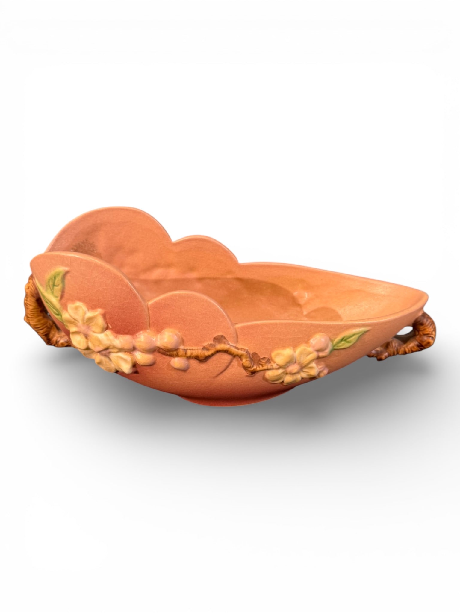 Roseville Pottery “Magnolia” Double-Handled Bowl, Shape 329-10: Roseville Pottery double-handled bowl in the Magnolia pattern, featuring applied cream-colored blossoms with soft pink shading and green leaves against a warm coral-to-rose ground. The low oval form i
