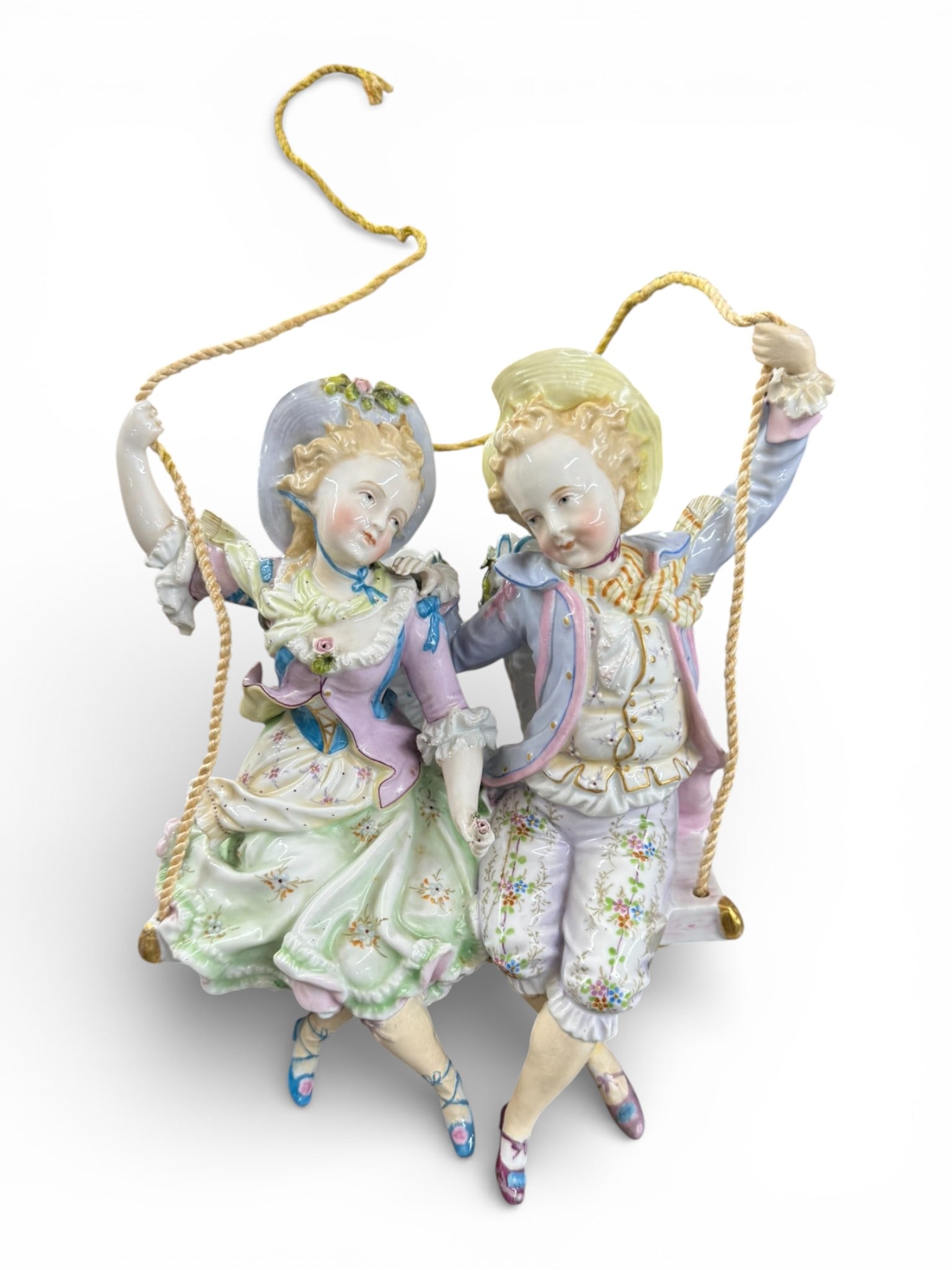 Continental Porcelain Figural Group of Boy and Girl on Swing: Charming Continental porcelain figural group depicting a finely modeled young boy and girl seated together on a rope swing, dressed in 18th century style costume with pastel enamel decoration, floral