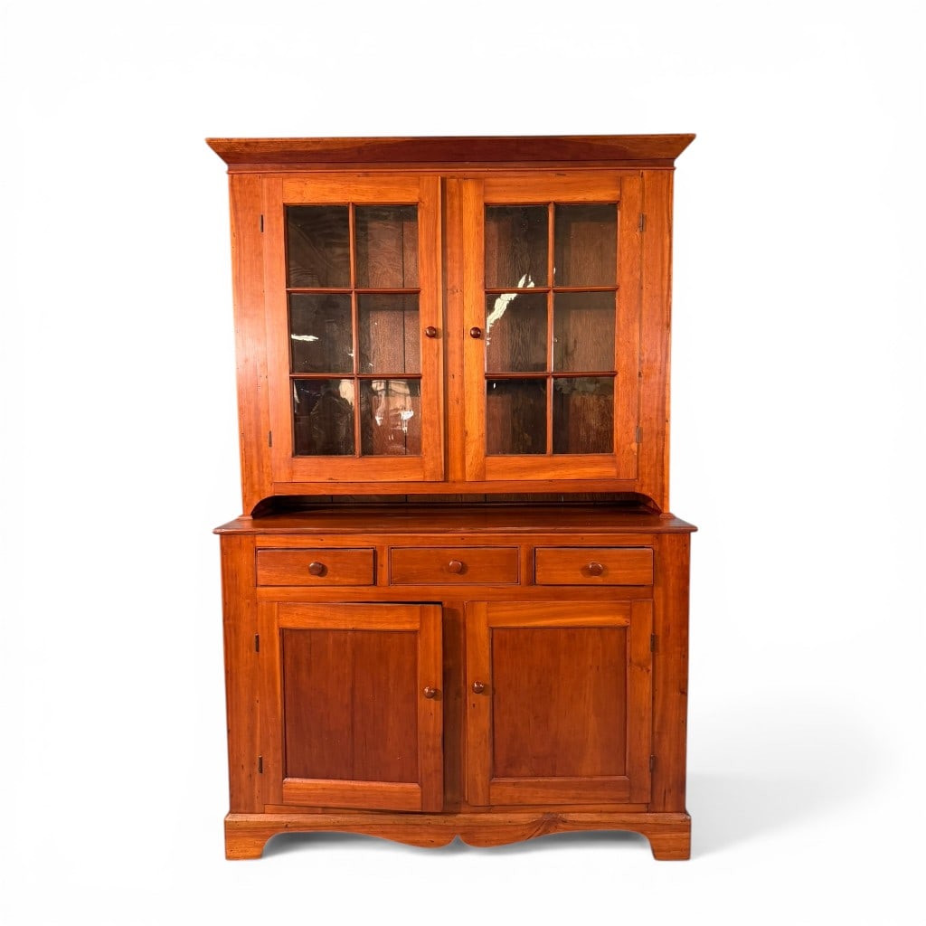 Pennsylvania Cherry Two-Part Cupboard: A well-proportioned Pennsylvania two-part cupboard in solid cherry, featuring a molded cornice above a glazed upper section with twelve-light doors retaining original wavy glass. The interior displays