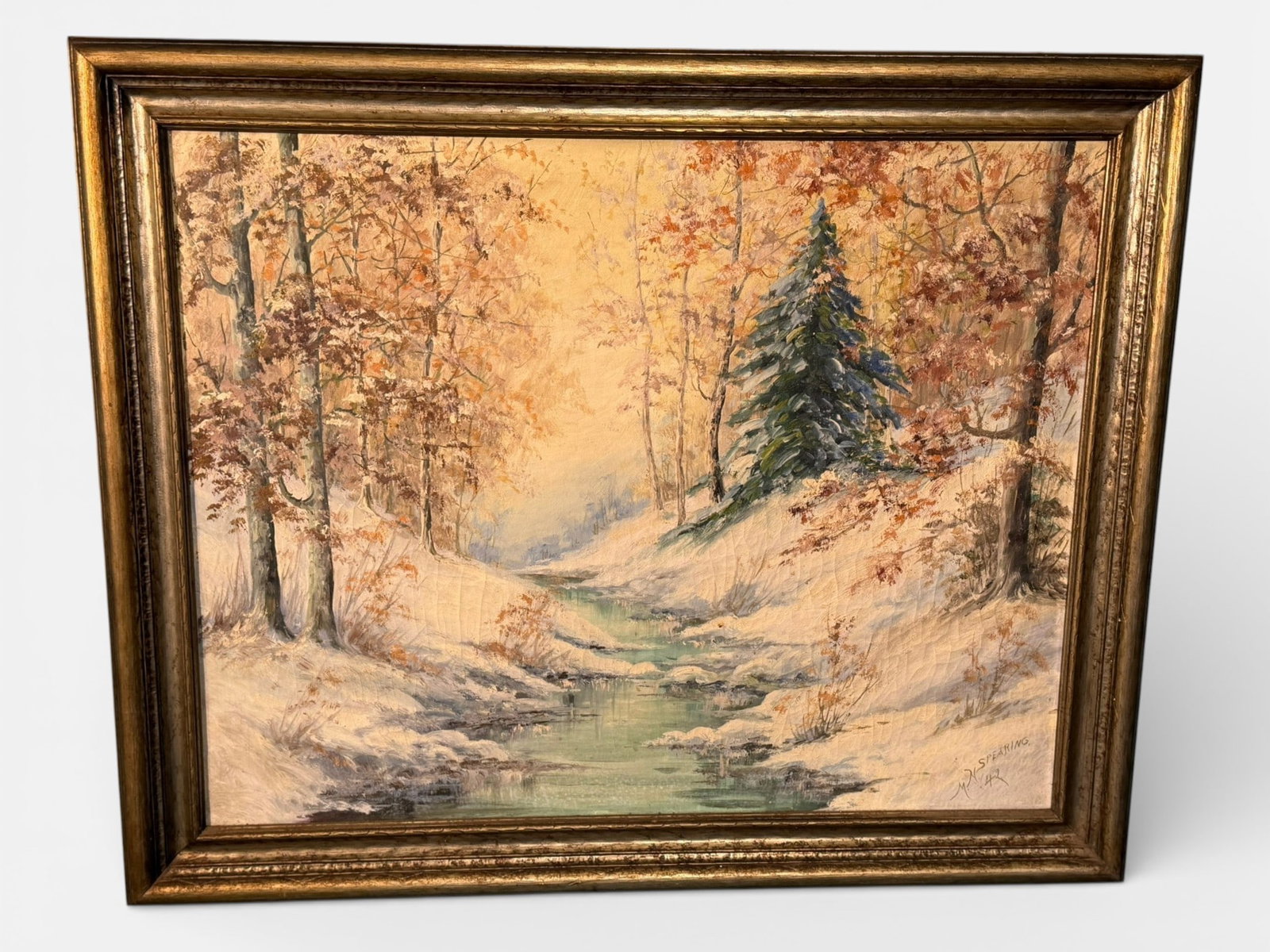 American School Oil on Canvas Winter Creek Landscape, signed M.M. Spearing\: Oil on canvas depicting a tranquil winter creek winding through a snow-covered woodland landscape, with autumnal foliage lingering on surrounding trees and a central evergreen anchoring the compositio
