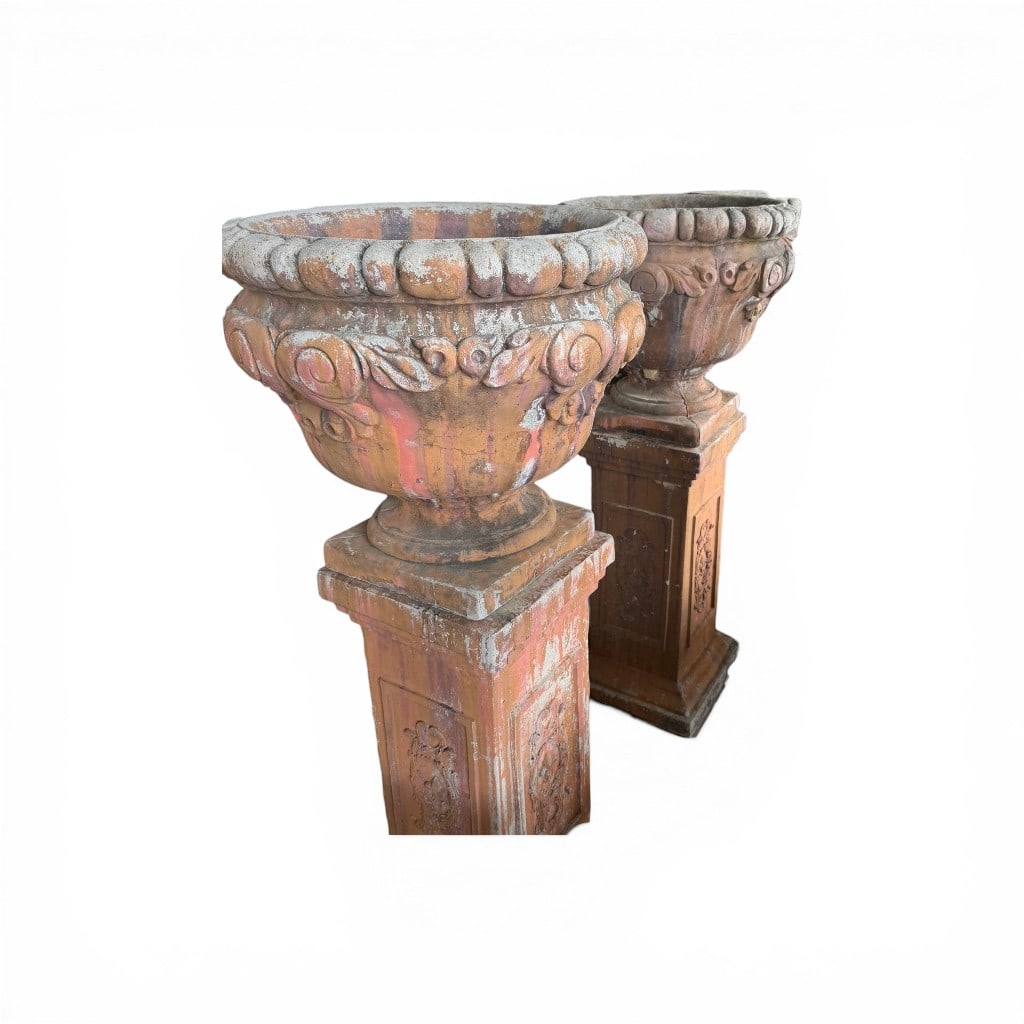 Pair of Monumental Terracotta Garden Urns on Pedestals: An impressive pair of monumental terracotta garden urns, each raised on a square-form pedestal base and richly modeled in the classical taste. The urns feature a bold gadrooned rim above a deep bowl