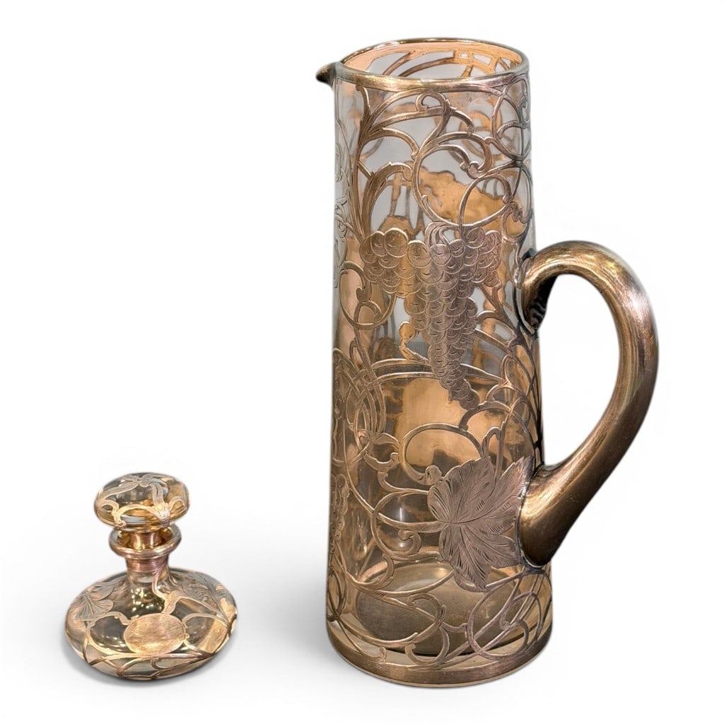 Art Nouveau Silver Overlay Glass Pitcher and Dresser Bottle: Art Nouveau clear glass pitcher with silver overlay grapevine, leaf, and foliate decoration, applied handle, and pinched spout, together with a matching or similar silver overlay clear glass dresser b