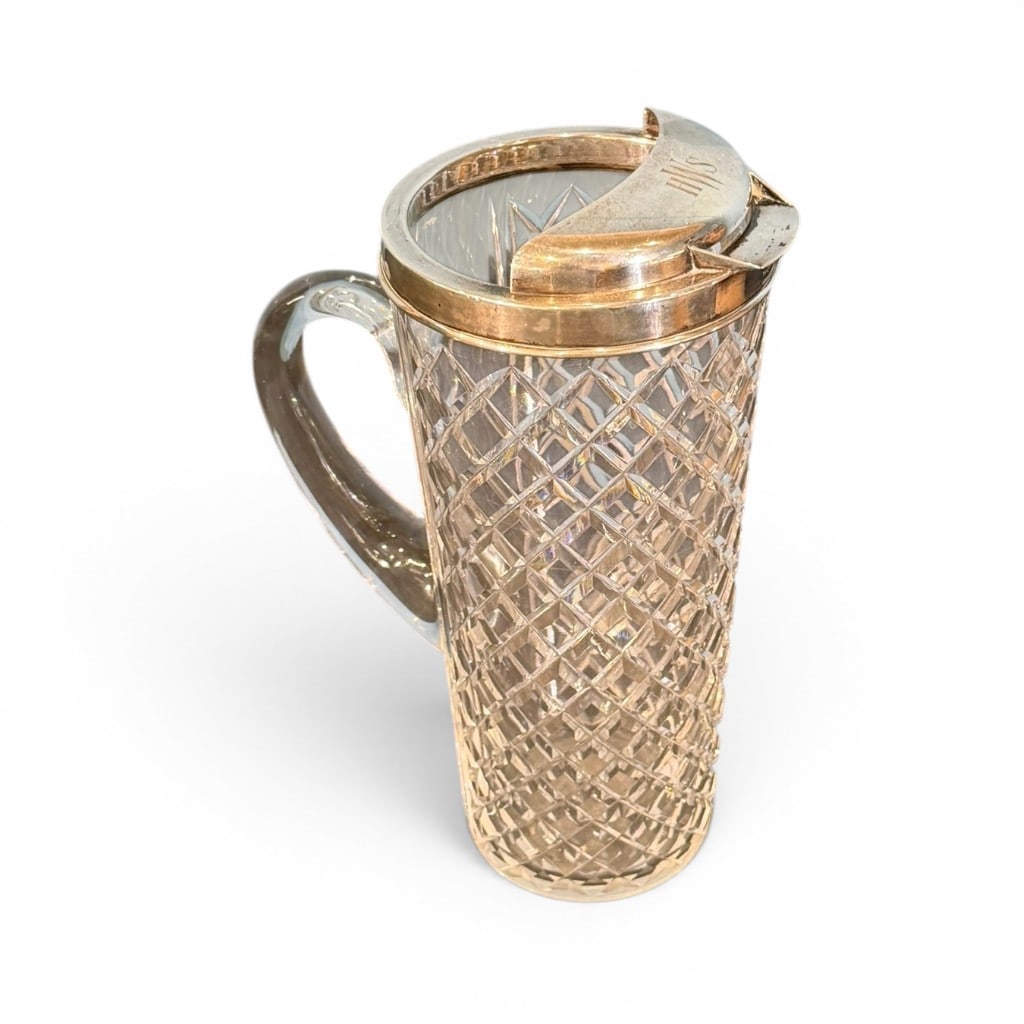 Tiffany & Co. Sterling Silver Mounted Cut Glass Cocktail Shaker, c. 1920: A Tiffany & Co. Art Deco period sterling silver mounted cut glass cocktail shaker or pitcher, circa 1920, the tall cylindrical cut glass body with diamond and crosshatched cutting, applied glass handl