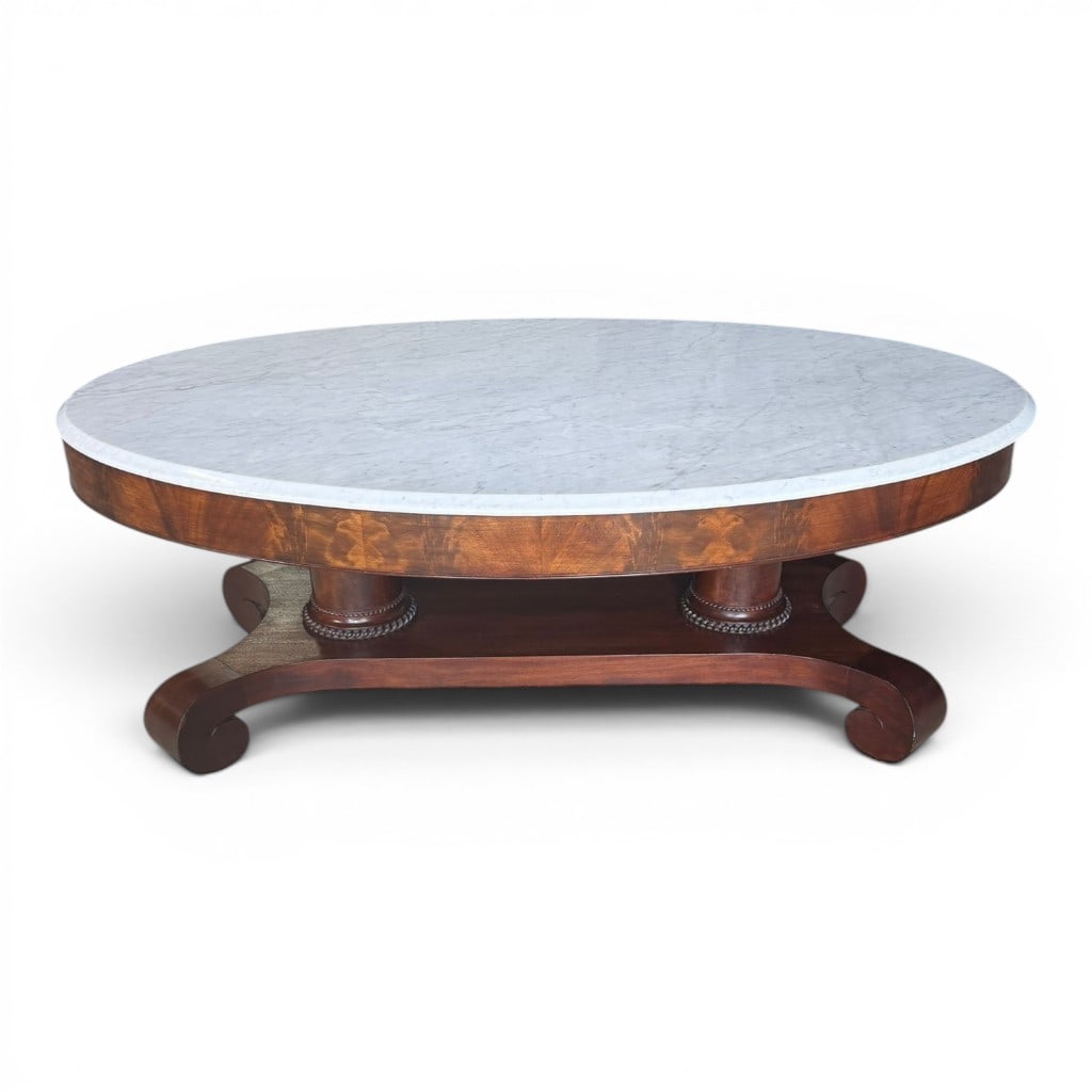 American Empire-Style Marble-Top Coffee Table: American Empire-style marble-top coffee table, likely adapted from a period or later 19th-century form, featuring an oval white marble top over a figured mahogany apron, raised on paired column