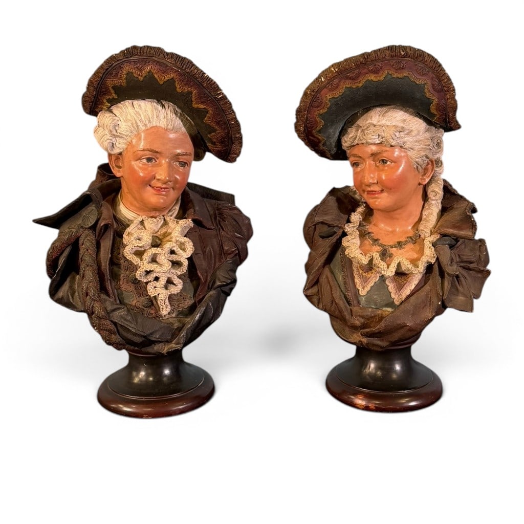 Pair Continental Polychrome Figural Busts: Pair Continental polychrome figural busts depicting an 18th-century gentleman and lady in period dress, each with tricorne-style hat, molded lace and costume detail, and raised on circular black and