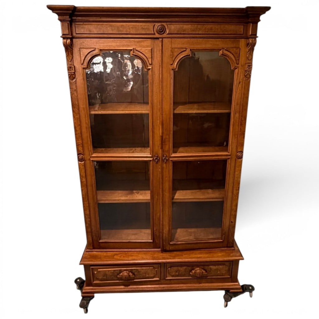 Victorian Walnut Two-Door Bookcase: A Victorian walnut bookcase, late 19th century, of tall rectangular form with a molded projecting cornice above two glazed doors, each with shaped arched upper molding and long glass panels. The case