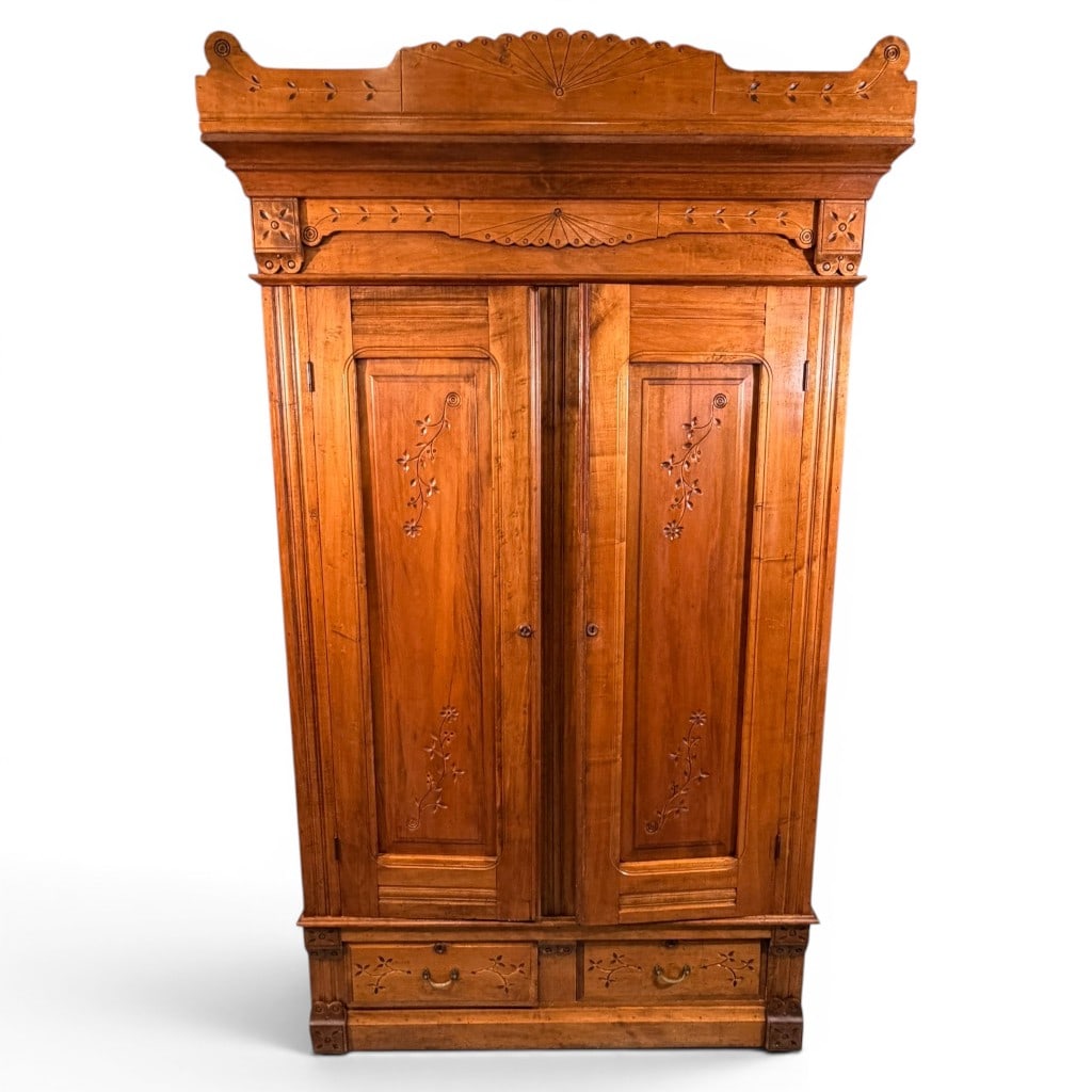 Victorian Eastlake Walnut Wardrobe: Victorian Eastlake wardrobe, American, late 19th century, in walnut with lighter figured secondary panels and carved floral and fan decoration throughout. The tall architectural case features a