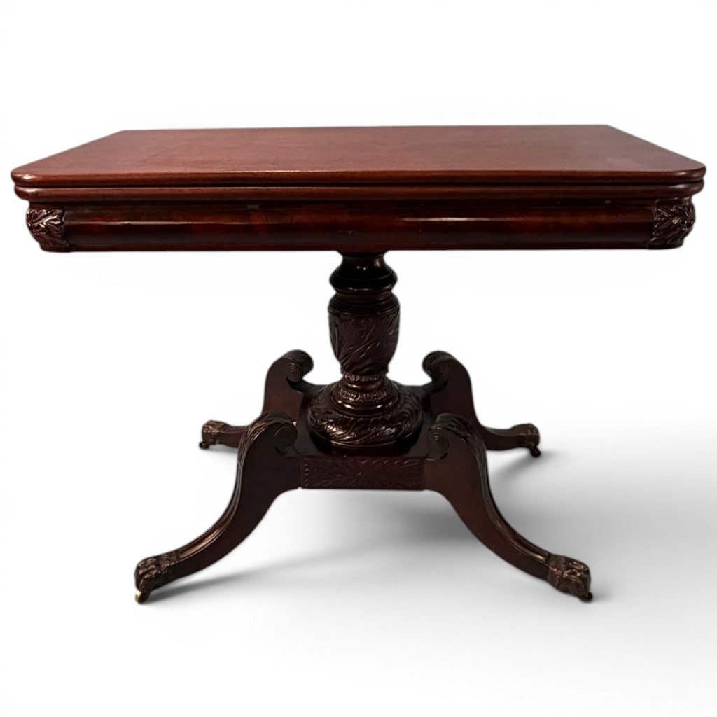 American Classical Mahogany Card Table with Acanthus-Carved Pedestal, 19th C.: An American Classical mahogany card table, 19th century, having a rectangular hinged fold-over top with rounded corners above a molded apron with carved corner blocks, raised on a boldly carved