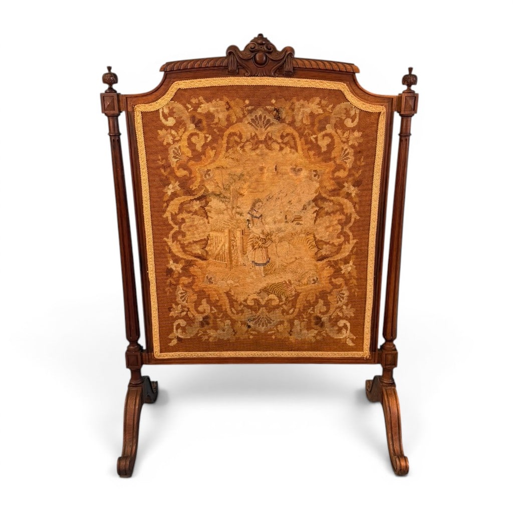 Victorian Needlepoint Firescreen, Late 19th Century: A Victorian needlepoint firescreen, late 19th century, having a shaped carved walnut or walnut-finished frame with a central needlework panel depicting a pastoral figural scene within a scrolling flor