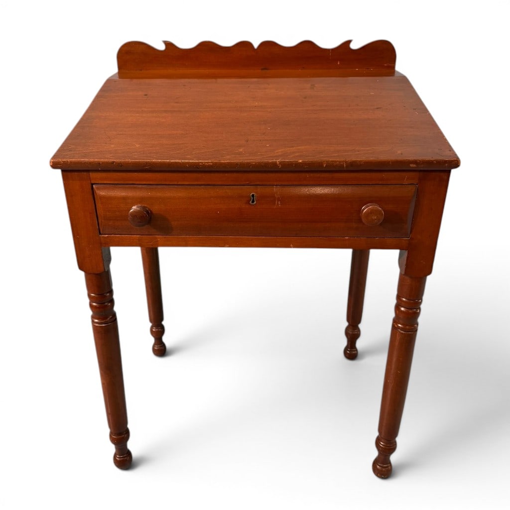 American Sheraton One-Drawer Work Stand with Backsplash, 19th Century: An American Sheraton one-drawer work stand, 19th century, having a rectangular overhanging top with shaped backsplash, single long drawer with wooden pulls and escutcheon, and turned legs ending in sm