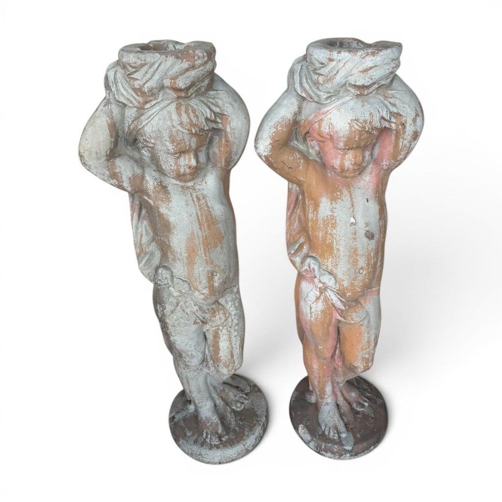Pair of Cast Stone Figural Cupid Garden Planters: Pair of cast stone garden figures modeled as standing putti or cupids, each supporting a planter-form vessel above the head, raised on integral circular bases. The figures retain traces of old