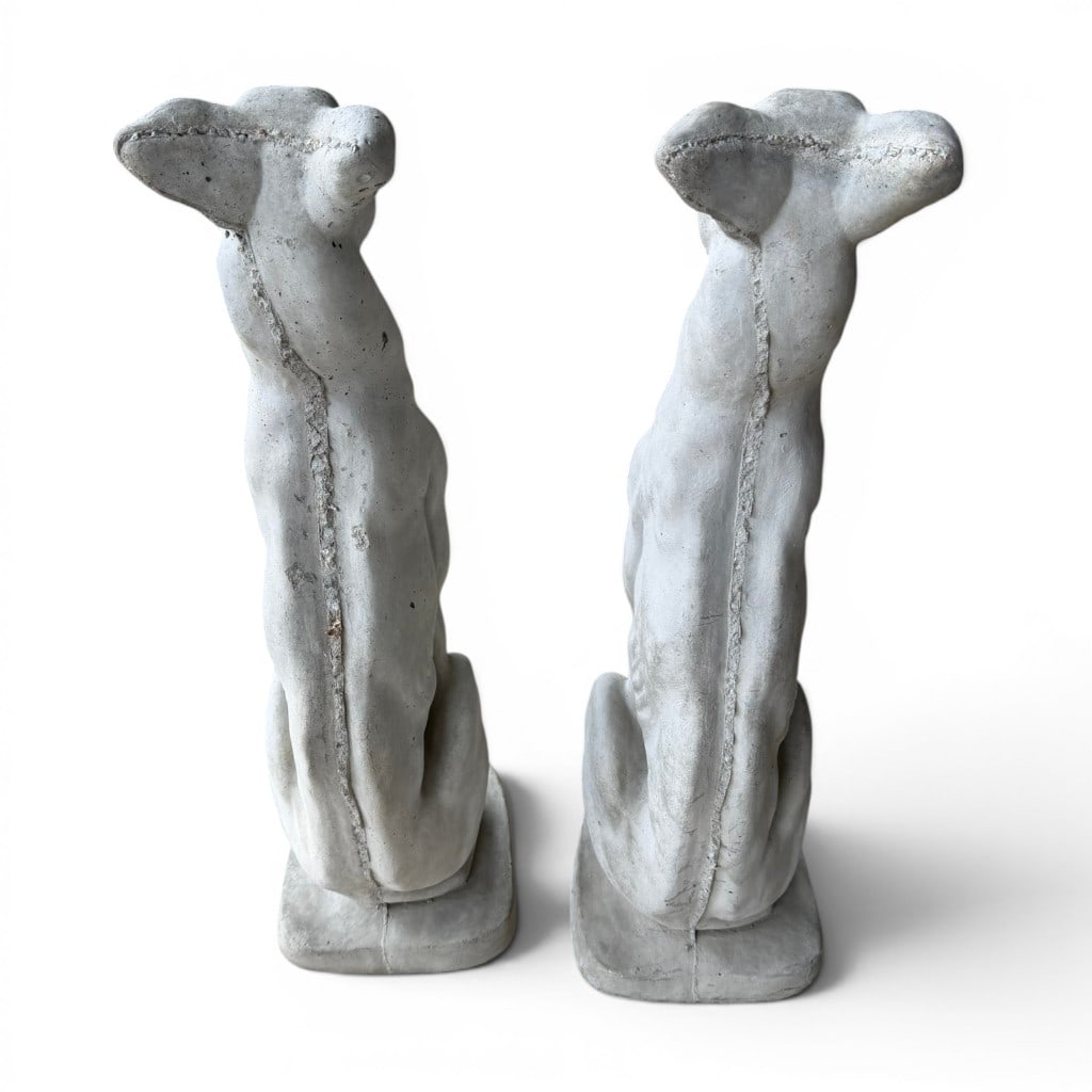 Pair of Garden Stone Dog Figures: Pair of garden stone dog figures, each modeled seated on an integral rectangular base with long neck, stylized head, folded ears, and attentive expression. The pair has a weathered white painted or ca