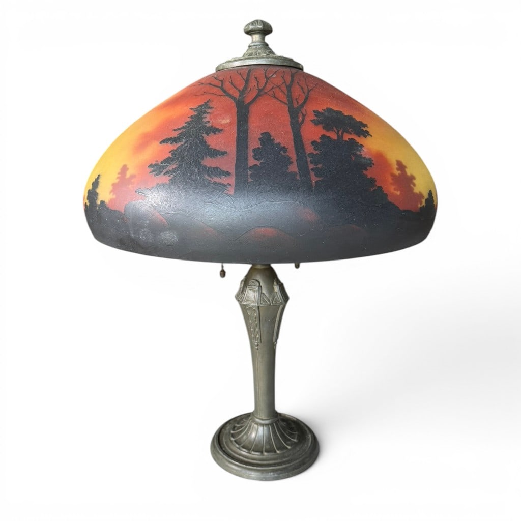 Reverse Painted Scenic Glass Table Lamp: Reverse painted scenic glass table lamp, early to mid 20th century style, having a domed glass shade decorated with a sunset landscape and silhouetted trees, raised on a patinated metal base with flut