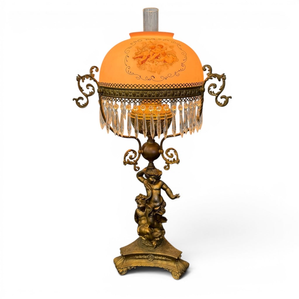 Victorian Figural Parlor Lamp with Pink Painted Shade: Victorian figural parlor lamp, having a pink domed glass shade decorated with painted cherub reserves and scroll borders, fitted within an ornate metal gallery with pendant prisms. The patinated metal
