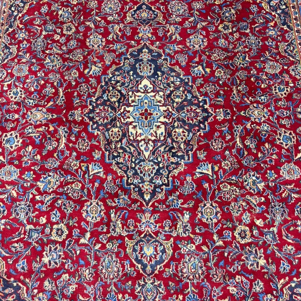 Hand Knotted Persian Kashan Carpet, 12 ft 7 in x 9 ft 7 in: Hand knotted Persian Kashan carpet, having a red field with central medallion, navy corner spandrels, and dense floral vine and palmette decoration, within a dark blue main border and multiple blue,
