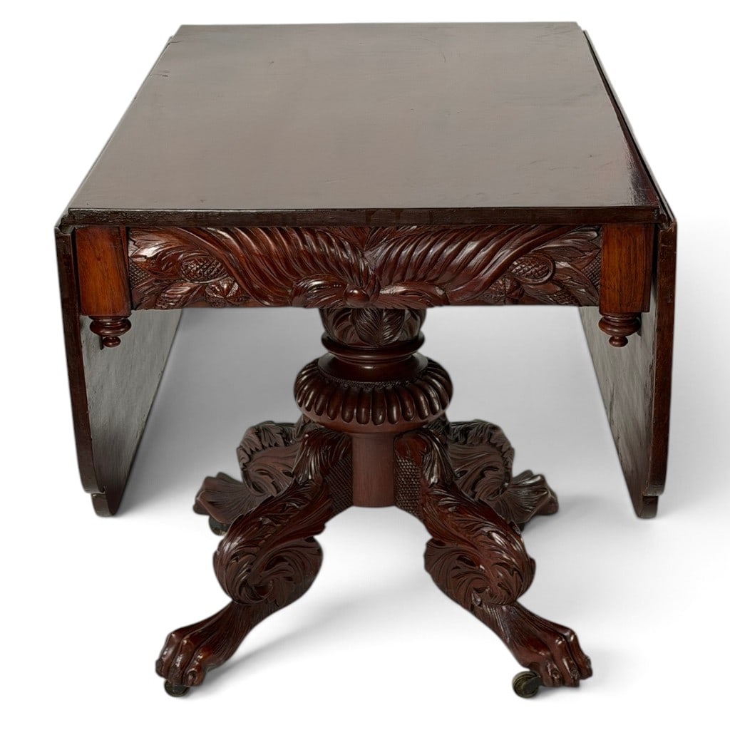 New York Classical Carved Mahogany Table: Origin: Probably New York CityDate: Circa 1835-1845Period/Style: Late American ClassicalMaterials: Mahogany, figured mahogany veneer, and brass castersForm: Drop-leaf breakfast or center tableDescript