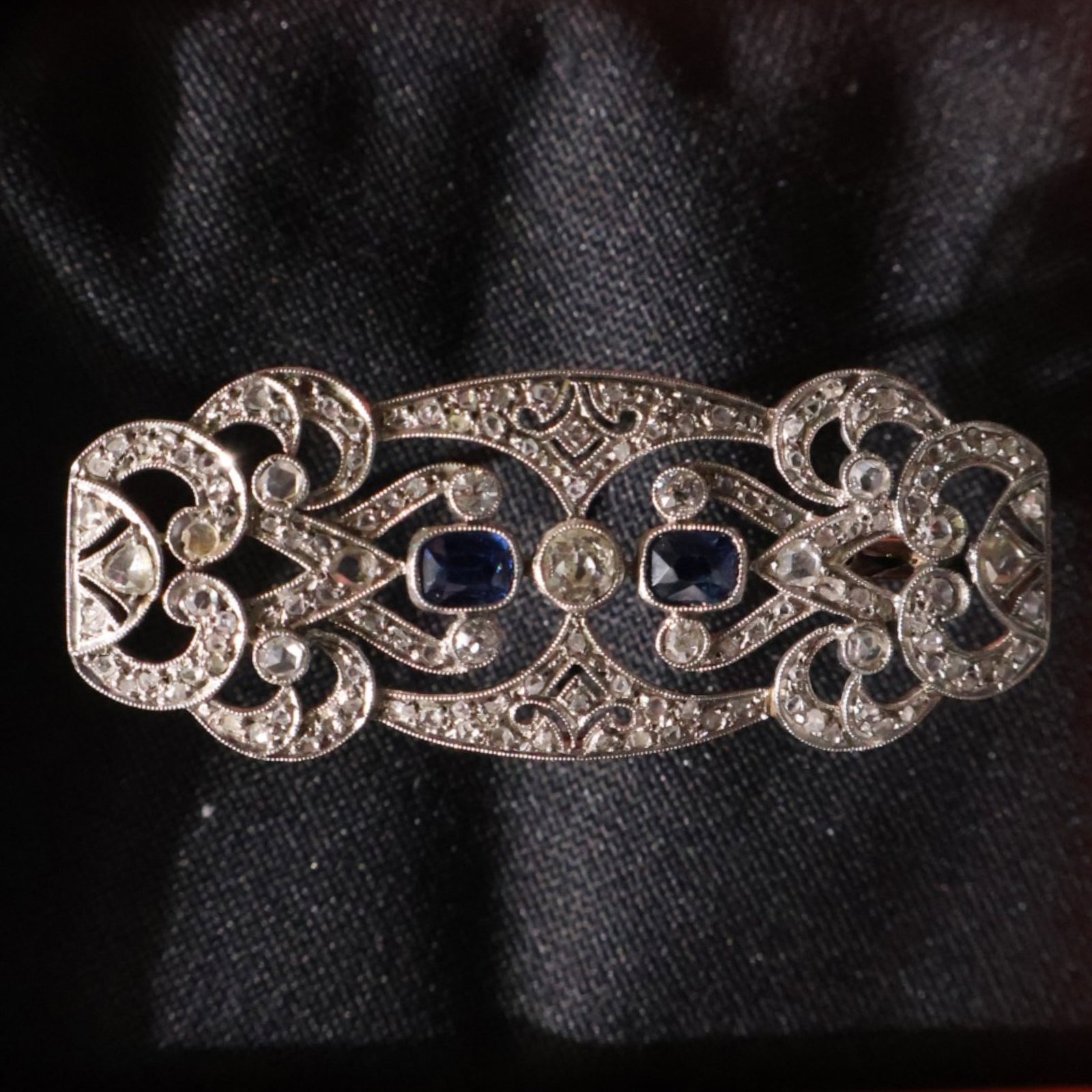 Platinum Sapphire and Diamond Brooch: Date: Late 20th to early 21st century Materials: Platinum, sapphires, and diamonds Form: Brooch Description: An elongated platinum openwork brooch centered by blue sapphires amid scrolling