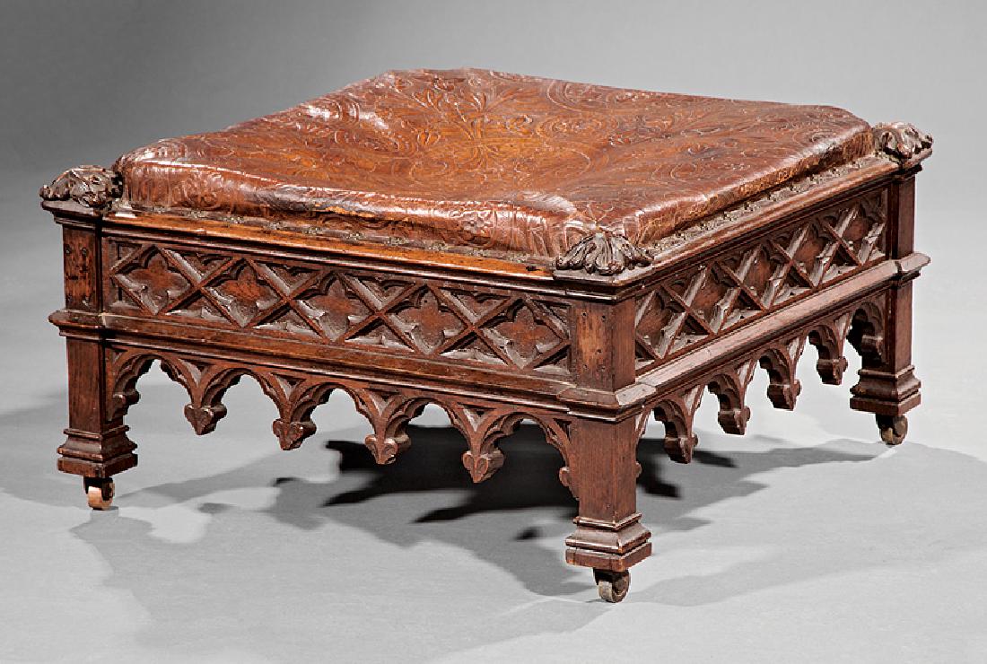 American Gothic Carved Oak Footstool: American Gothic Carved Oak Footstool, c. 1880, New York, leather cushion, foliate corners, quatrefoil frieze, square legs and feet, casters, old paper label, h. 15 1/2 in., w. 29 in., d. 29 in. Proven