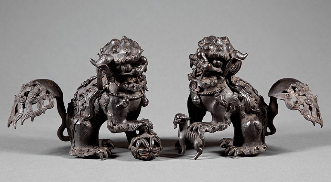 Chinese Cast Metal Figures of Buddhist Lions: Pair of Chinese Cast Metal Figures of Buddhist Lions, each modeled crouching, the male with its right paw resting on a brocade ball, the female with hers on a cub, h. 8 in., w. 9 3/4 in, Provenance: S