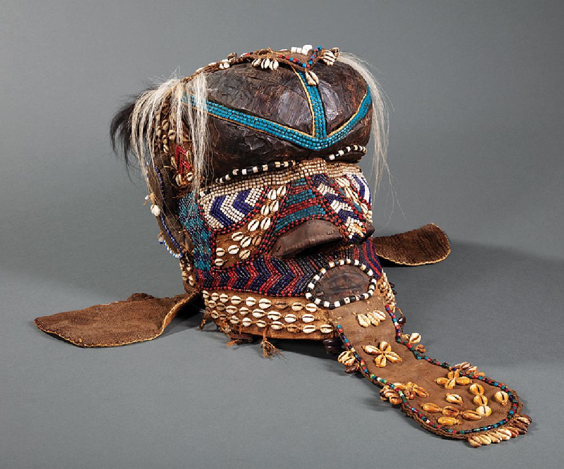 African Embellished Carved Wood Bwoom Helmet Mask: African Bead, Cowrie Shell, Fur, Hair, Seedpod, Cloth, Hide, and Copper Embellished Carved Wood Bwoom Helmet Mask, Kuba, DRC, h. 20 3/4 in., w. 9 1/2 in. d. 12 1/2 in. Provenance: Memphis Brooks Museu