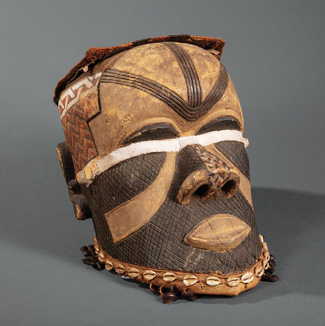 African Giphogo/Kipoko Mask from Chief's Treasury: African Carved and Painted Wood Giphogo/Kipoko Mask from the Chief's Treasury, Pende, Zaire, ornamented with cowrie shells, seed pods, hide, and raffia, h. 14 in., w. 10 7/8 in., d. 17 in. Provenance: